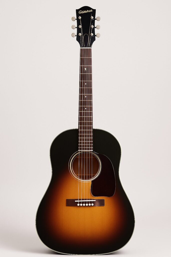 alt="エピフォン J-45 アコースティックギターを縦に立てた状態で撮影した画像。ビンテージ感のある外観とバランスの取れたフォルムが視認できる。"